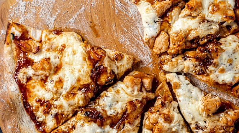 Close-up of a BBQ chicken pizza with melted cheese and sauce on a wooden board.